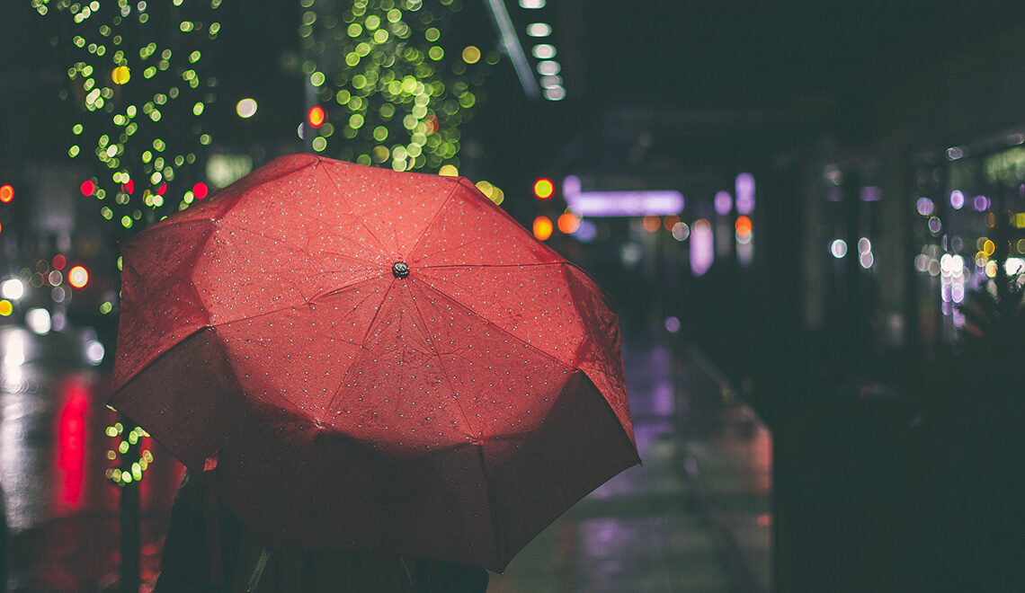 Synkkä syysää ja punaisen sateenvarjon alla kulkeva ihminen